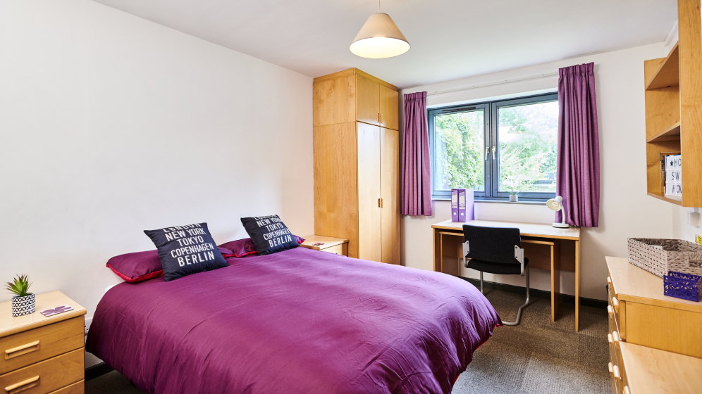 The master bedroom within the family and couple flats. There is a double bed, two bedside tables, a desk and chair, two sets of drawers, a wardrobe and some shelving.